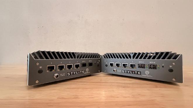 Zwei lüfterlose Protectli-Mini-PCs mit STYLITE- und Protectli-Branding nebeneinander auf einem Holztisch, jeweils vier RJ45-Ports und zwei SFP+-Slots